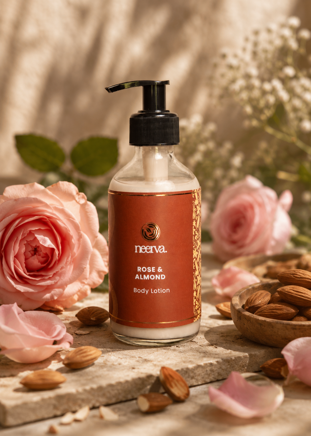 A bottle of Neerva Rose & Almond body lotion stands on a stone slab surrounded by pink roses, almonds, and soft floral props in a warm, sunlit setting.