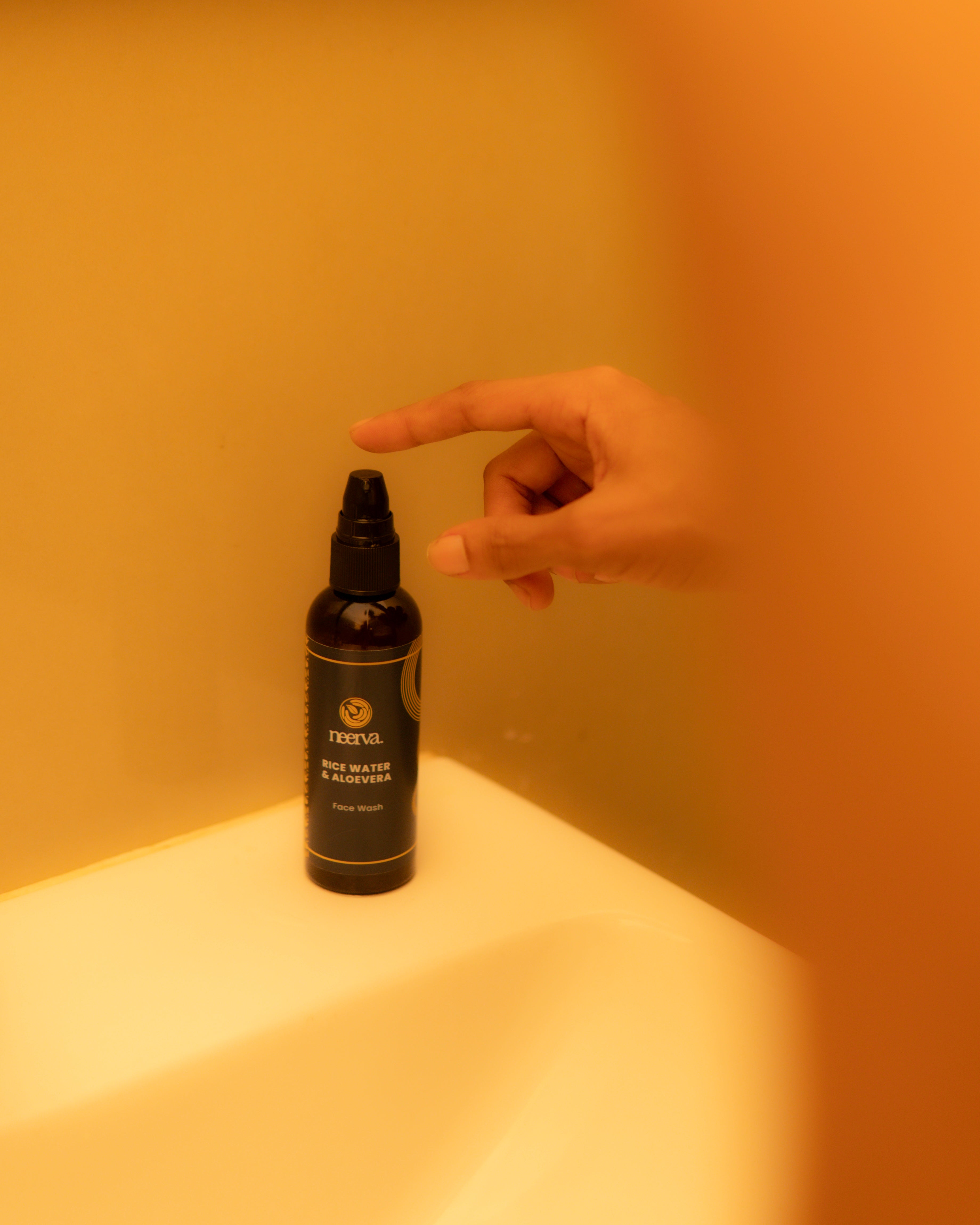 A small black spray bottle labeled Neerva on a white surface, with a hand pointing toward the top of the bottle in a warm yellow-toned indoor setting.