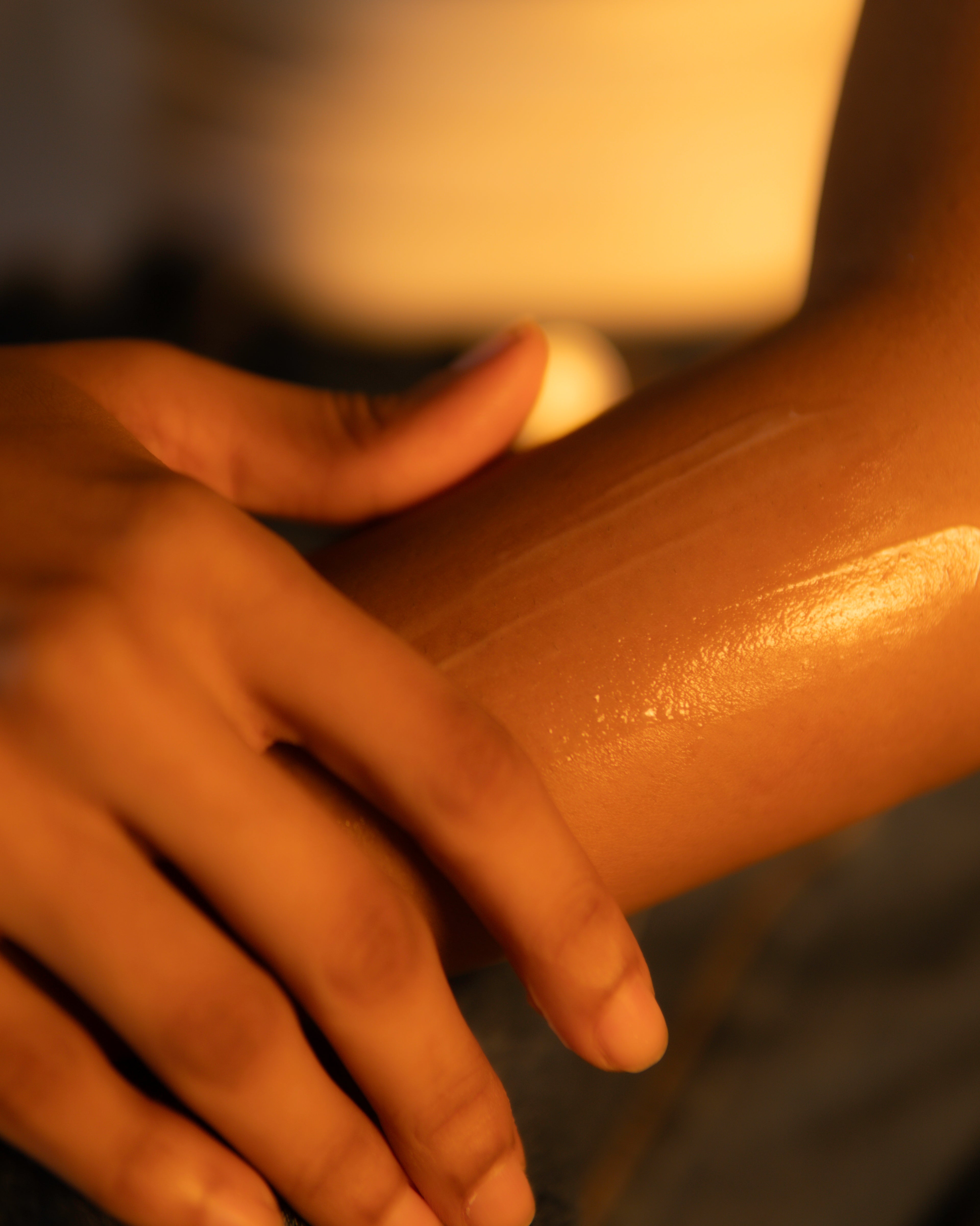Hand applying a lotion or cream to a person's arm with a warm glow.